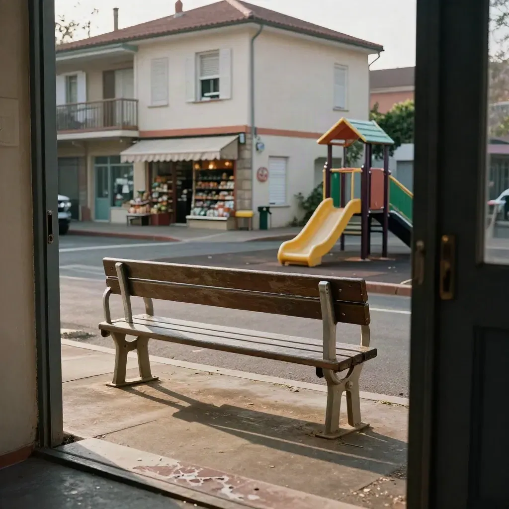 Rue de quartier vue d’une porte, banc, aire de jeux vide et épicerie floue au fond.